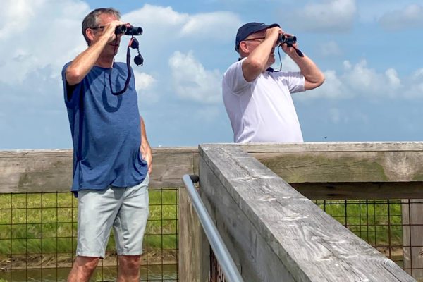 men looking through binoculars on a sea rim state park boardwalk in port arthur