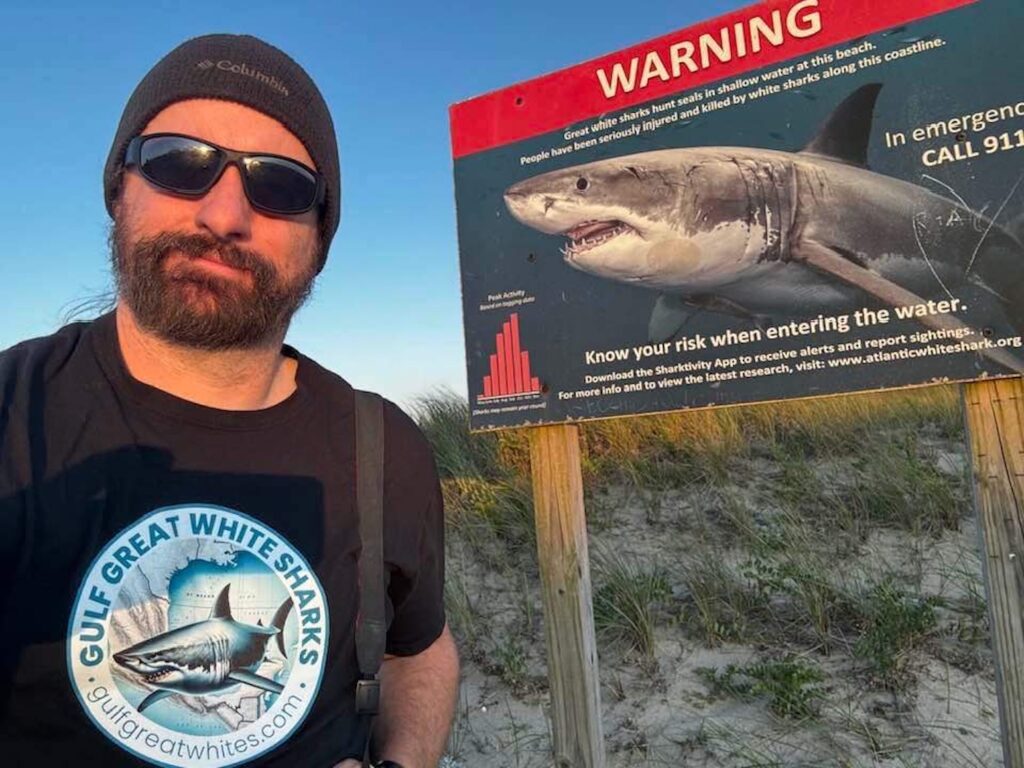 chester moore stands by a gulf great white shark sign